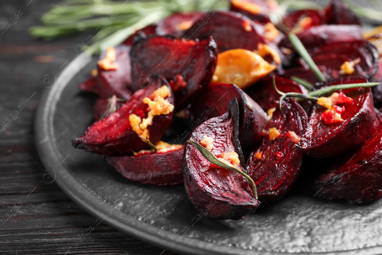 Photo of Roasted beetroot slices, garlic and rosemary on black wooden table, closeup