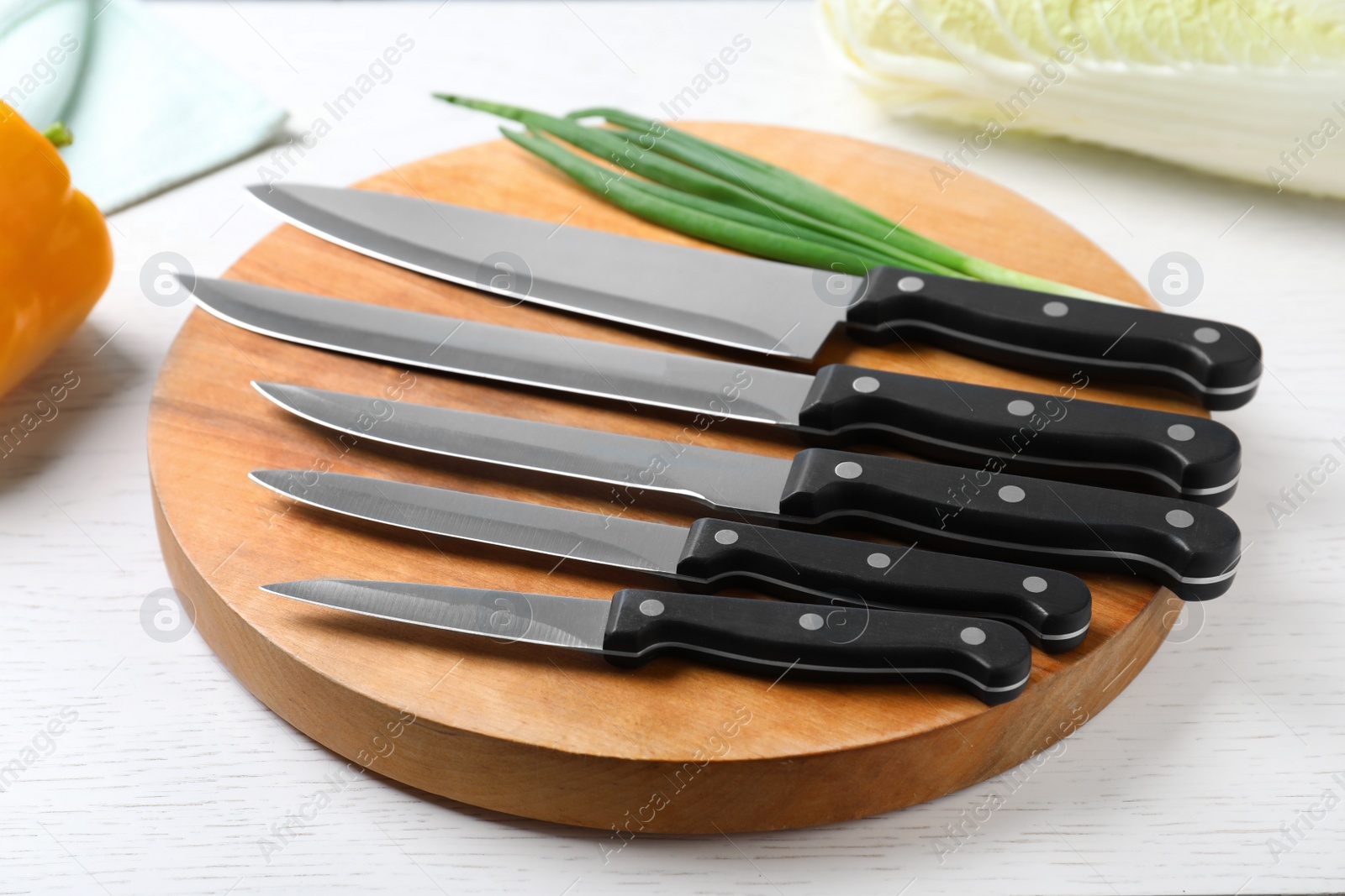 Photo of Cutting board with set of different knives and green onion on white wooden table