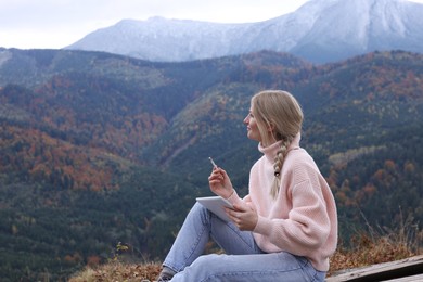 Photo of Young woman drawing on tablet in mountains, space for text