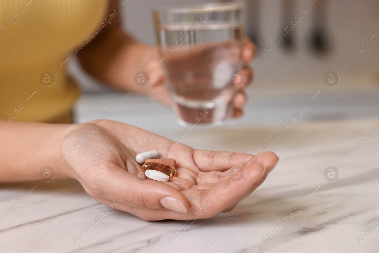 Photo of Woman with vitamin pills and glass of water at white marble table, closeup