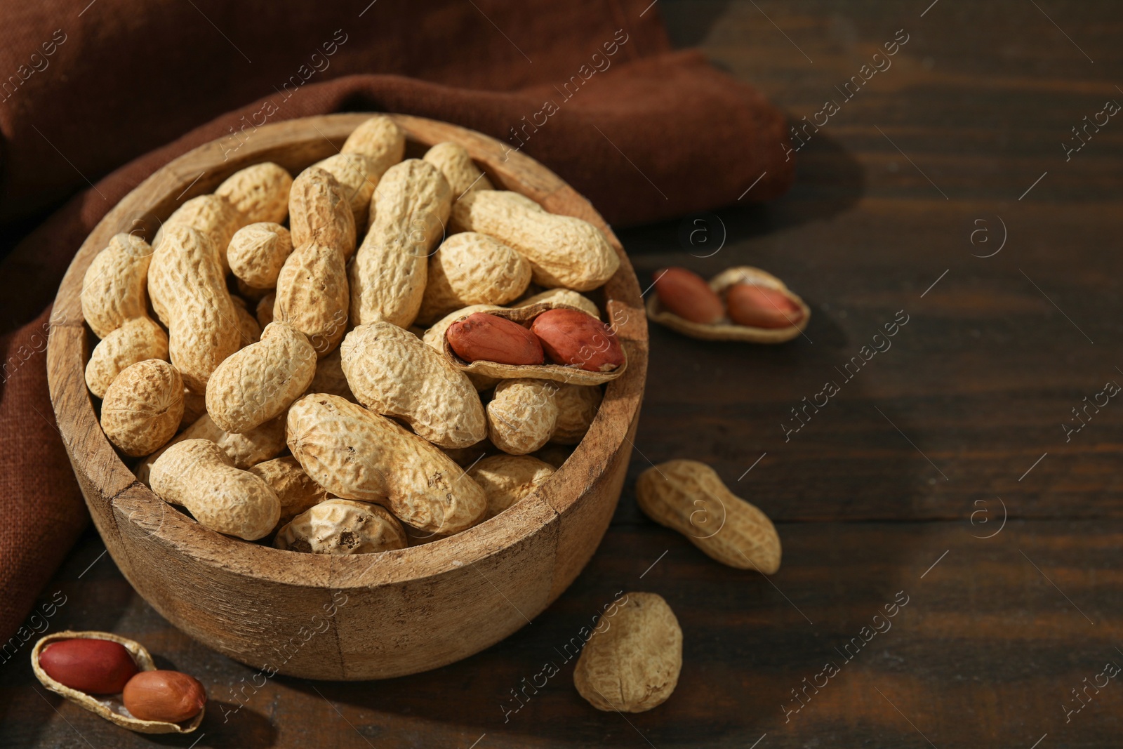 Photo of Fresh unpeeled peanuts in bowl on wooden table. Space for text