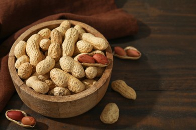 Fresh unpeeled peanuts in bowl on wooden table. Space for text