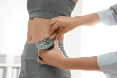 Photo of Nutritionist measuring woman's fat layer with caliper indoors, closeup