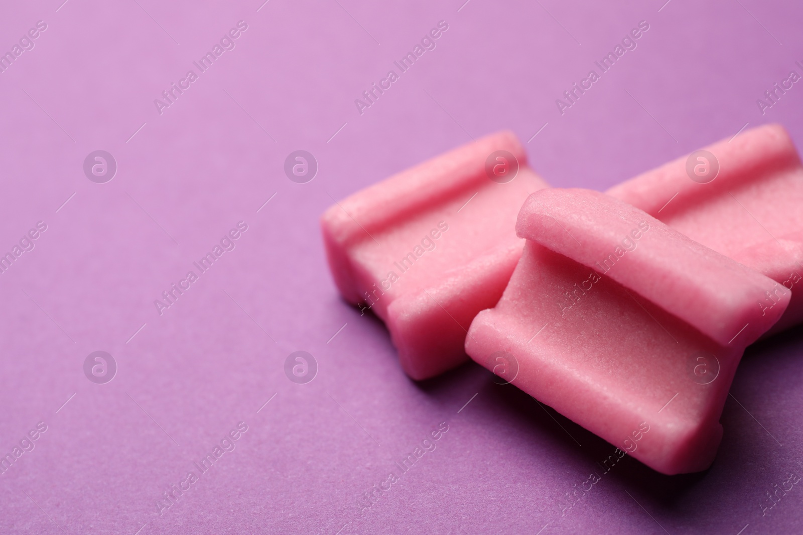 Photo of Tasty pink chewing gums on purple background, closeup. Space for text