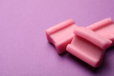 Photo of Tasty pink chewing gums on purple background, closeup. Space for text