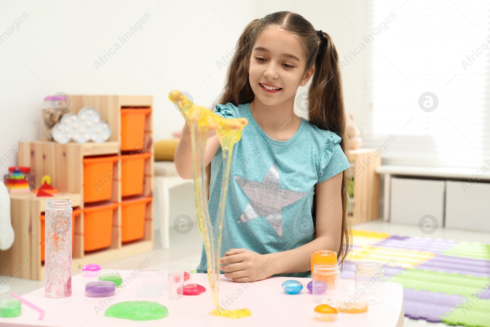 Photo of Preteen girl playing with slime at table indoors