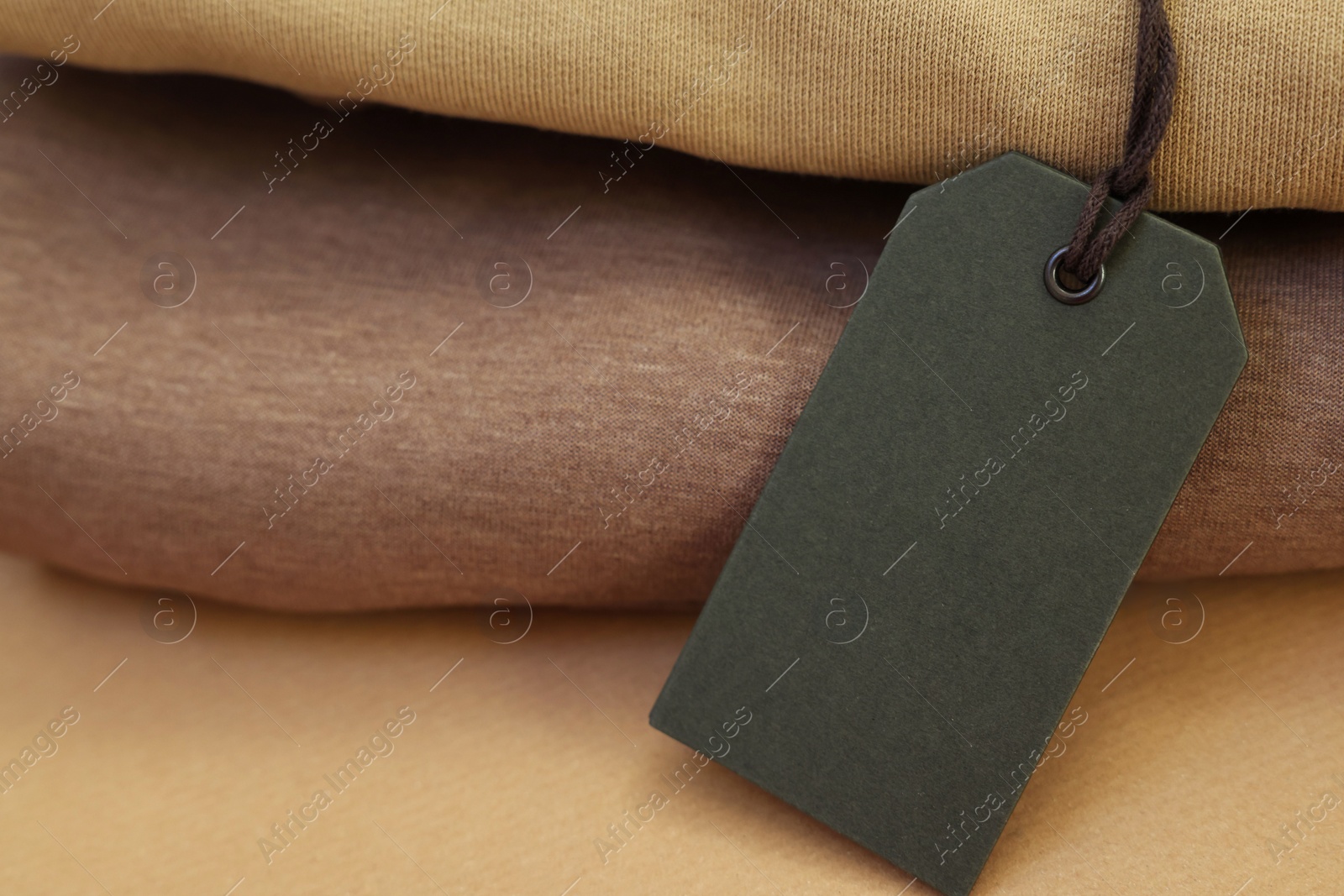 Photo of Garment with cardboard tag on kraft paper sheet, closeup. Space for text