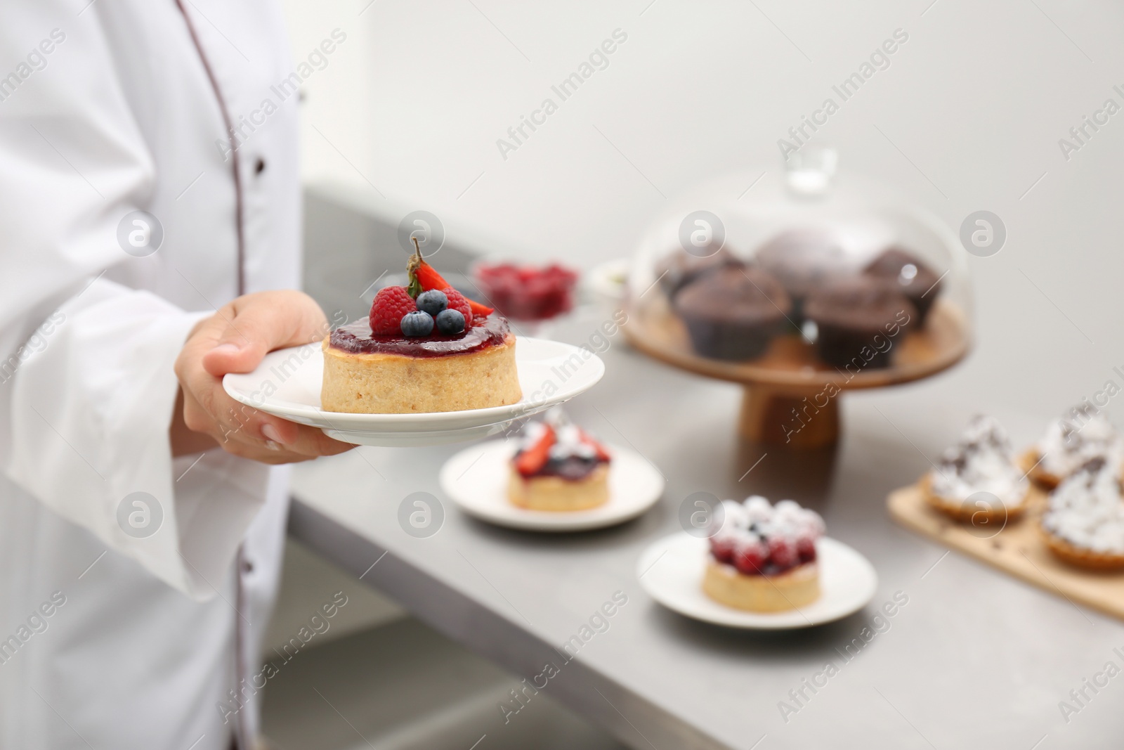 Photo of Woman holding plate with dessert in kitchen, closeup. Tasty pastry