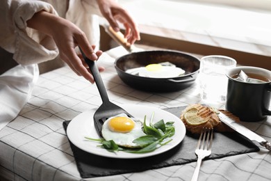 Photo of Woman putting tasty fried eggs onto plate at table indoors, closeup