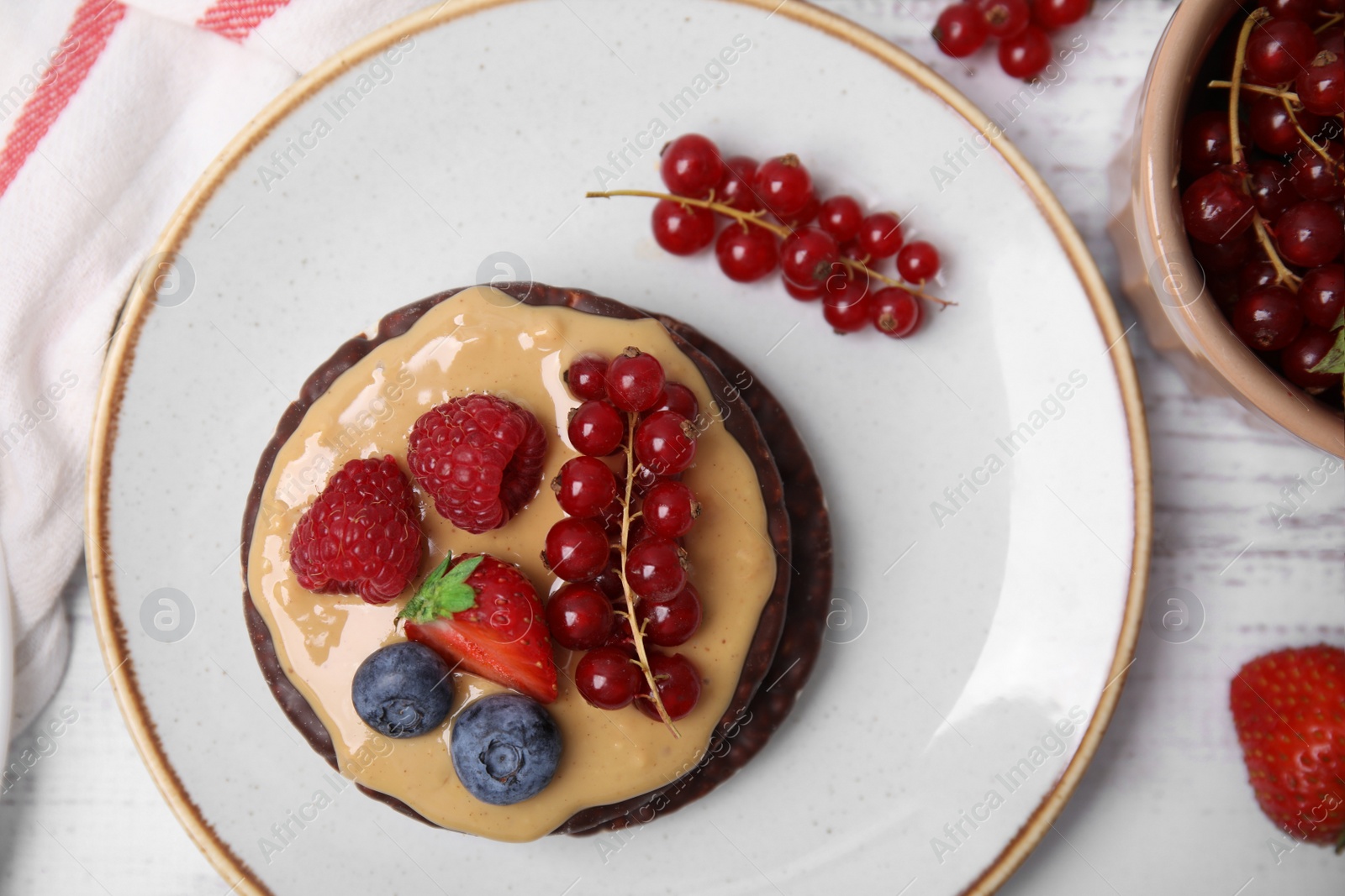 Photo of Crunchy rice cakes with peanut butter and sweet berries served on white wooden table, flat lay