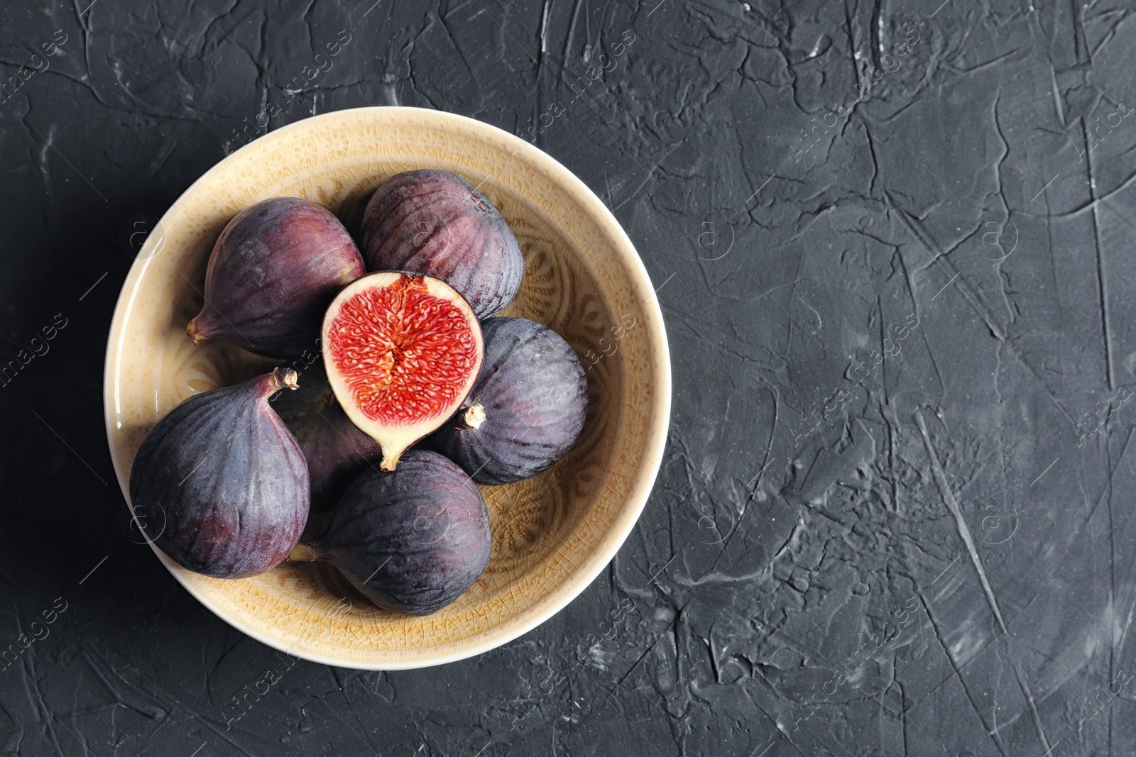 Photo of Bowl with fresh ripe figs on dark background, top view. Space for text