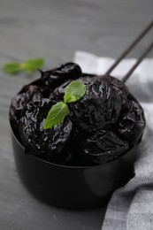 Sweet dried prunes and mint in scoop on grey wooden table, closeup