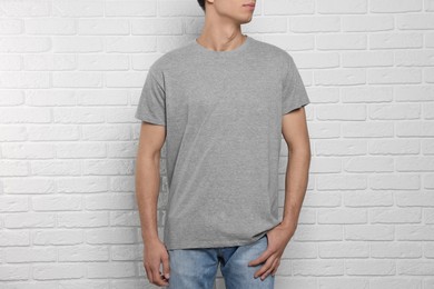Photo of Man wearing gray t-shirt near white brick wall, closeup. Mockup for design