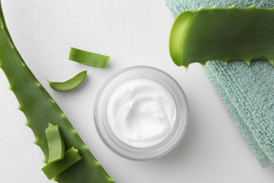 Jar with cream, cut aloe leaves and towel on white table, flat lay