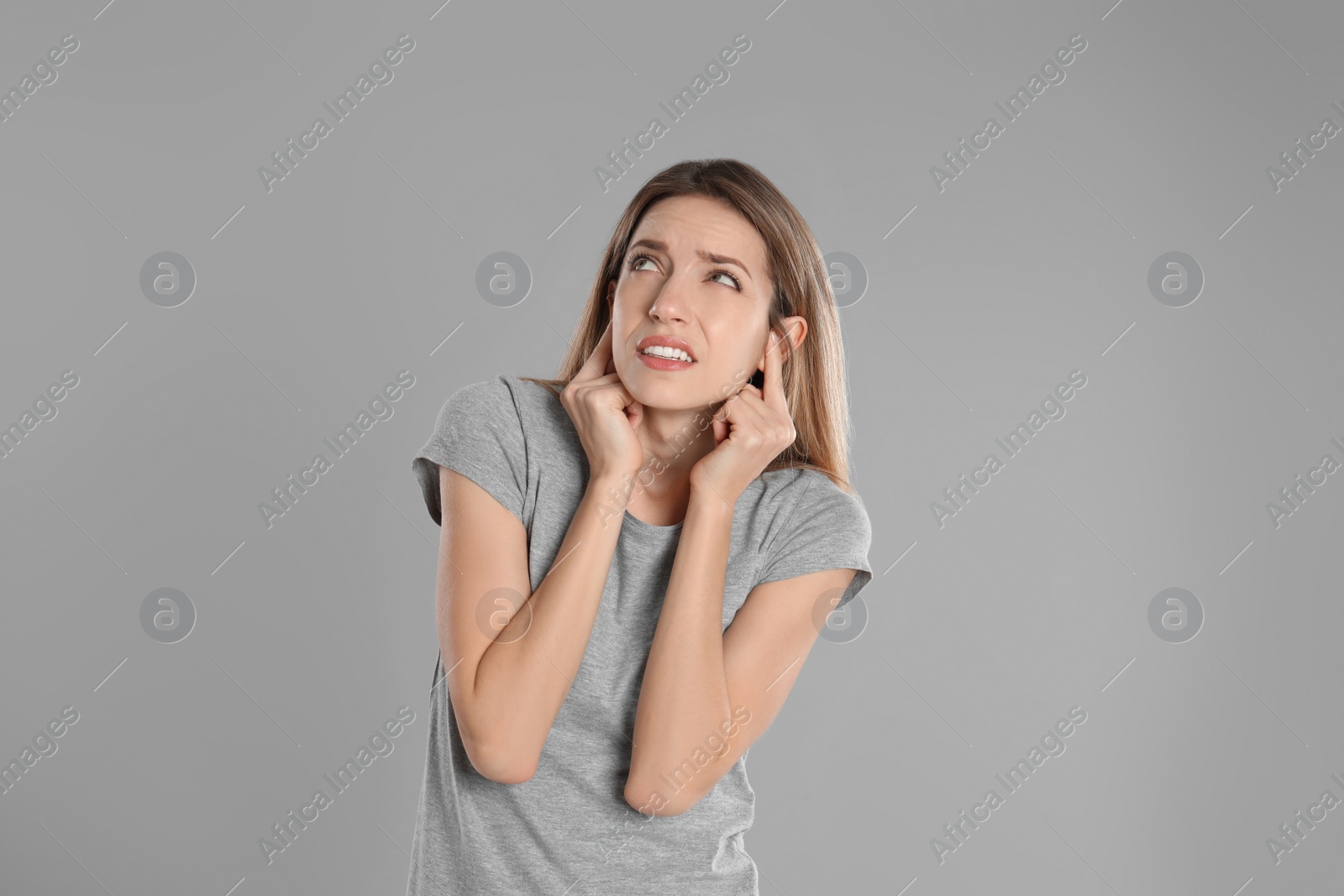 Photo of Emotional young woman covering her ears with fingers on grey background