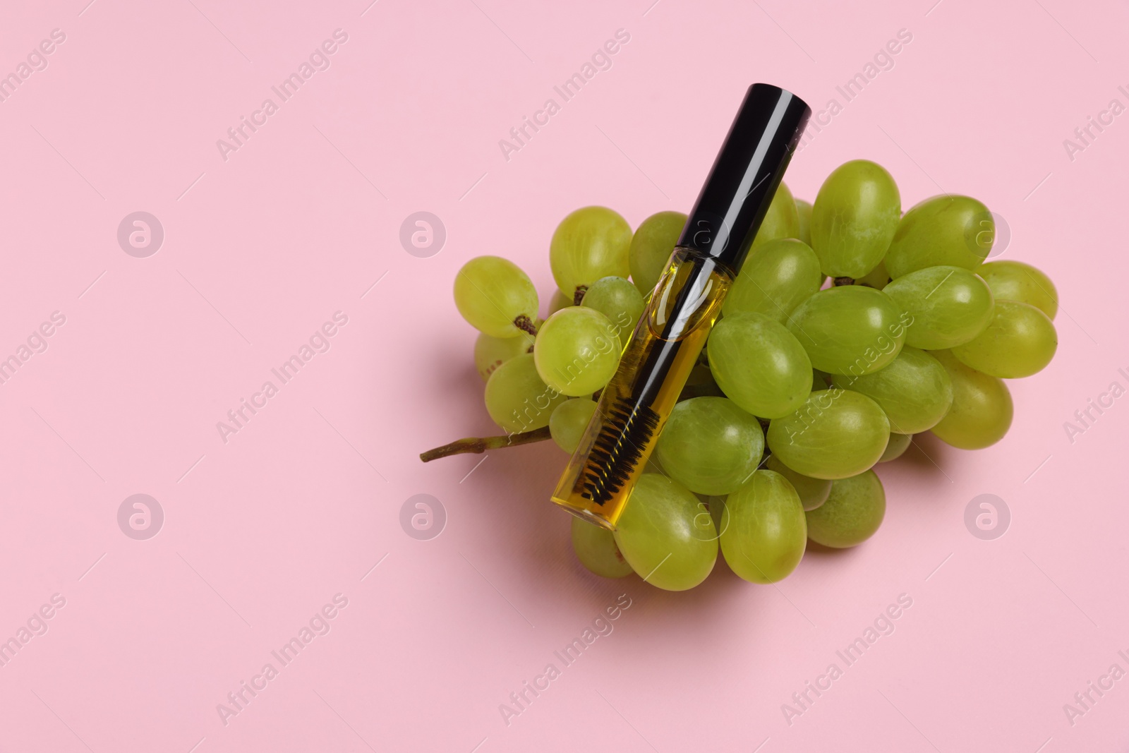 Photo of Tube of eyelash oil and fresh grape on pink background, top view