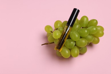 Tube of eyelash oil and fresh grape on pink background, top view