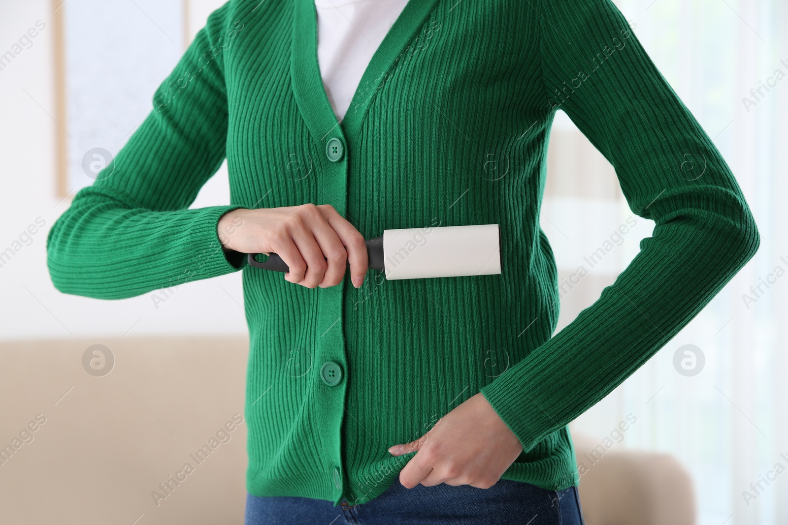 Photo of Woman cleaning green jacket with lint roller indoors, closeup