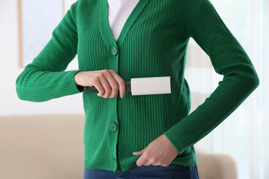 Woman cleaning green jacket with lint roller indoors, closeup