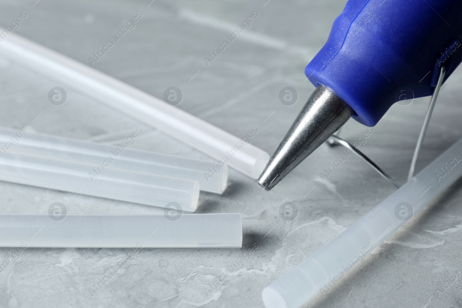 Photo of Hot glue gun and sticks on light grey marble table, closeup