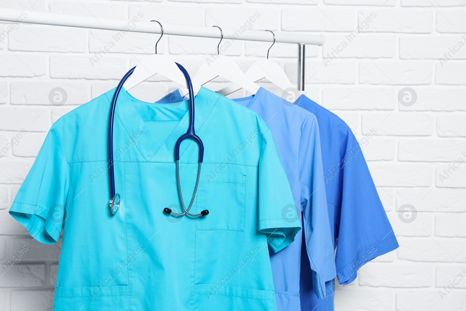 Photo of Medical uniforms and stethoscope hanging on rack near white brick wall