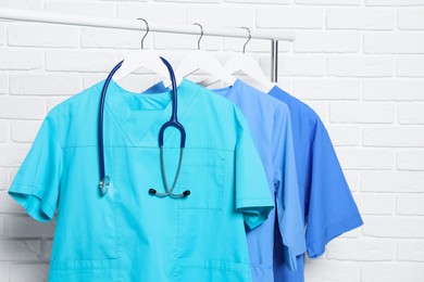 Photo of Medical uniforms and stethoscope hanging on rack near white brick wall