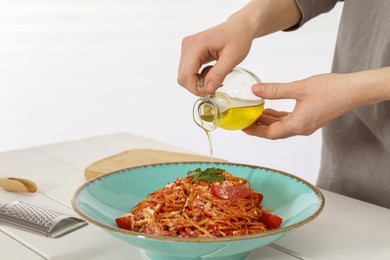 Photo of Food stylist pouring oil into spaghetti at white wooden table in photo studio, closeup