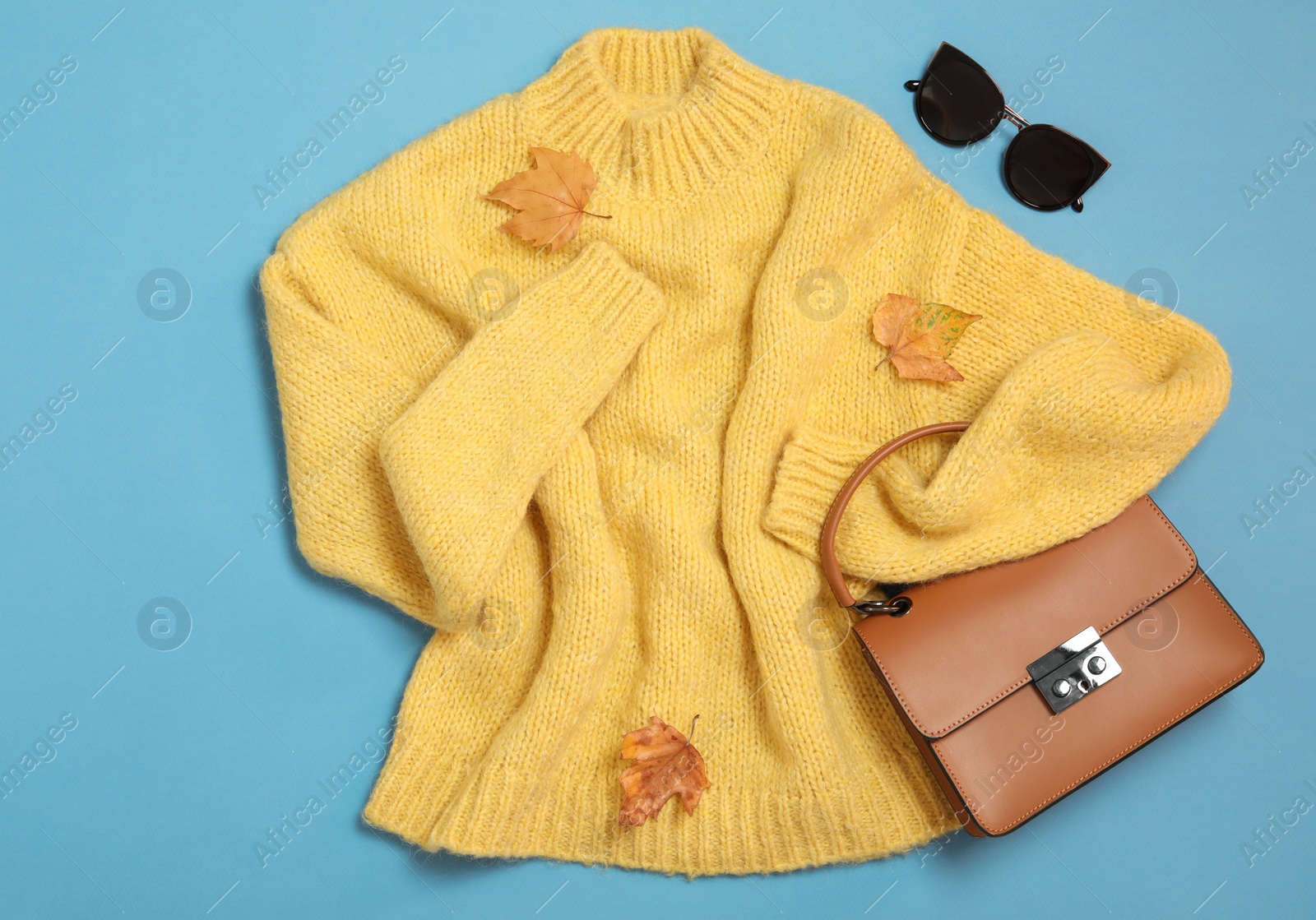 Photo of Flat lay composition with sweater and dry leaves on light blue background. Autumn season