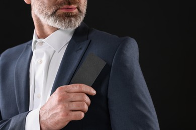 Photo of Businessman holding blank business card on black background, closeup