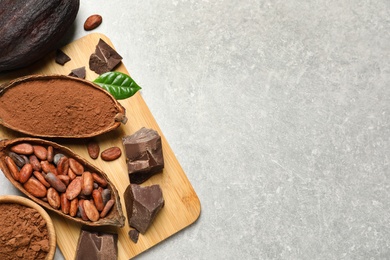 Flat lay composition with cocoa pods, powder and beans on light table. Space for text