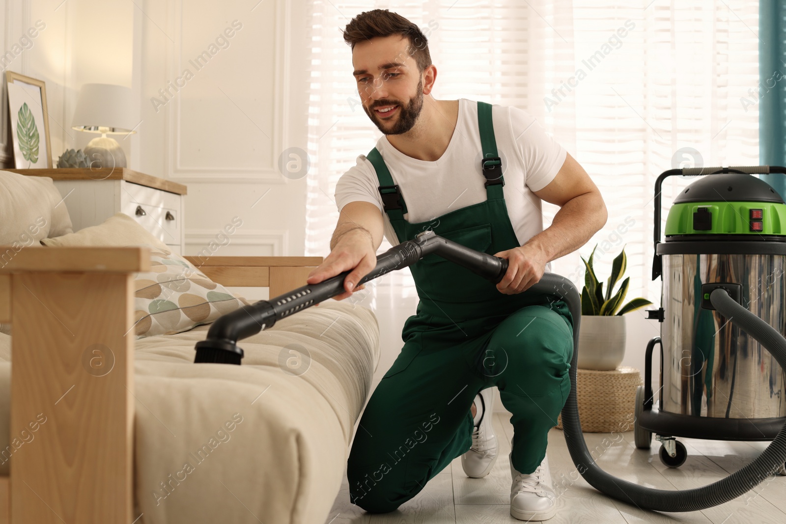 Photo of Professional janitor vacuuming sofa in living room