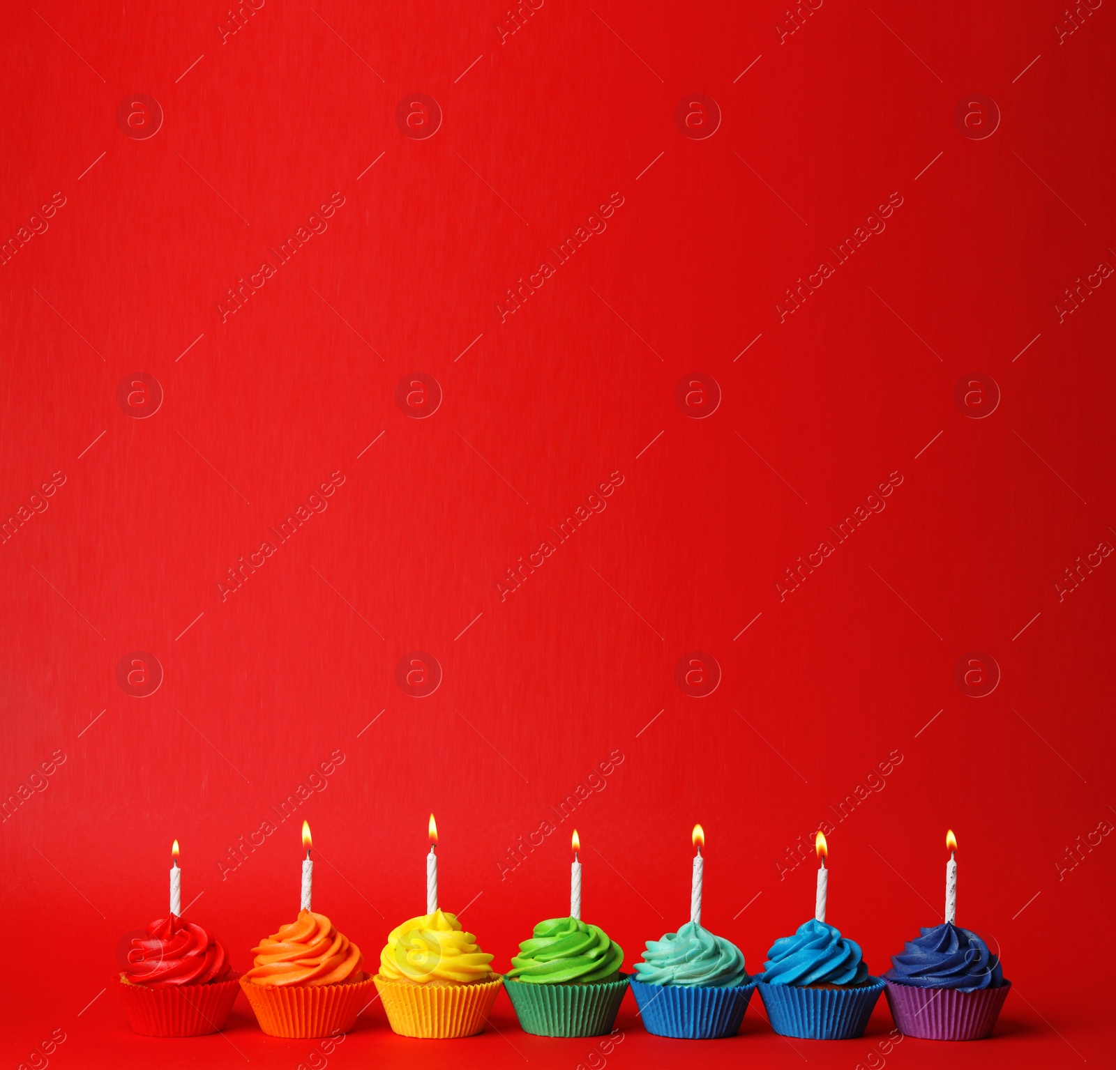 Photo of Delicious birthday cupcakes with candles on red background