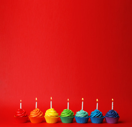 Photo of Delicious birthday cupcakes with candles on red background