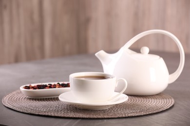 Photo of Aromatic tea in cup, saucer, teapot and dry flower petals on grey table