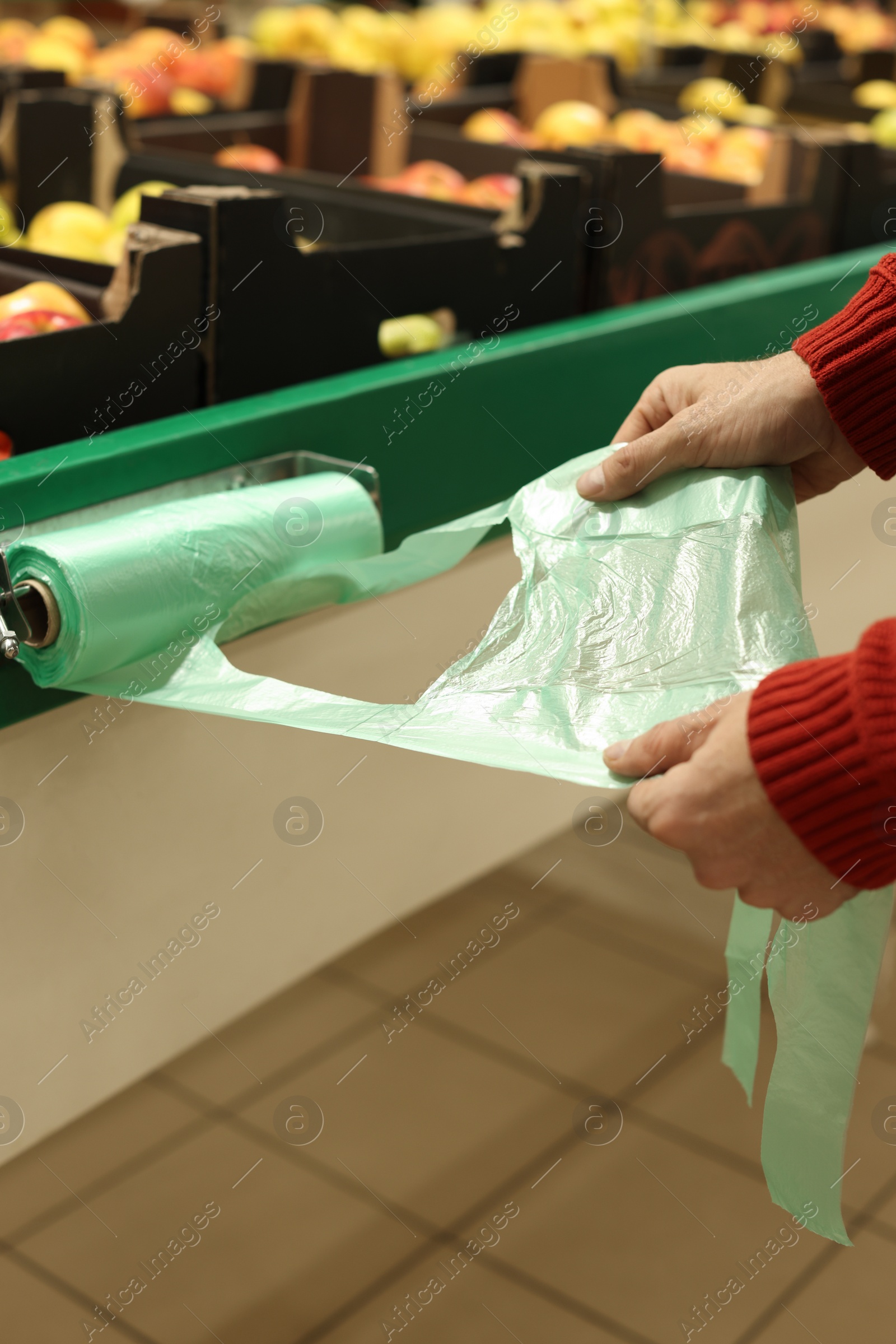 Photo of Man taking plastic bag from holder near crates with fruits in supermarket, closeup