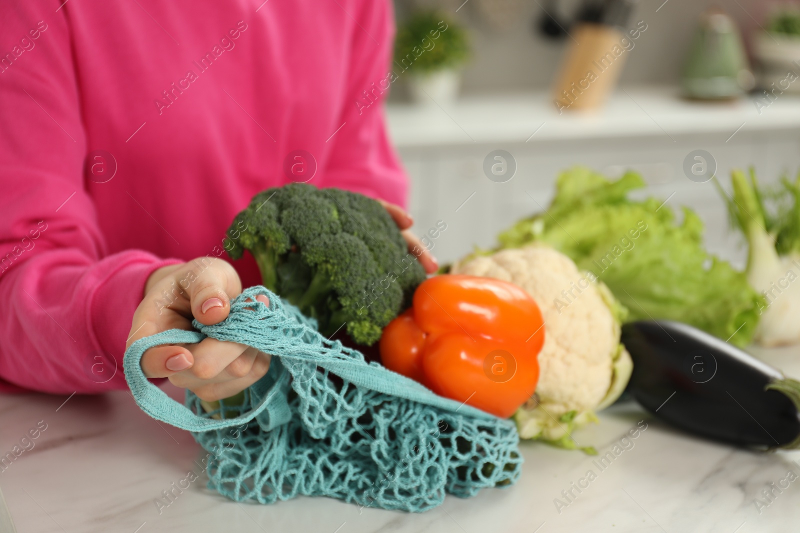 Photo of Woman with string bag of fresh vegetables at light marble table, closeup