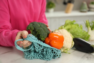 Woman with string bag of fresh vegetables at light marble table, closeup