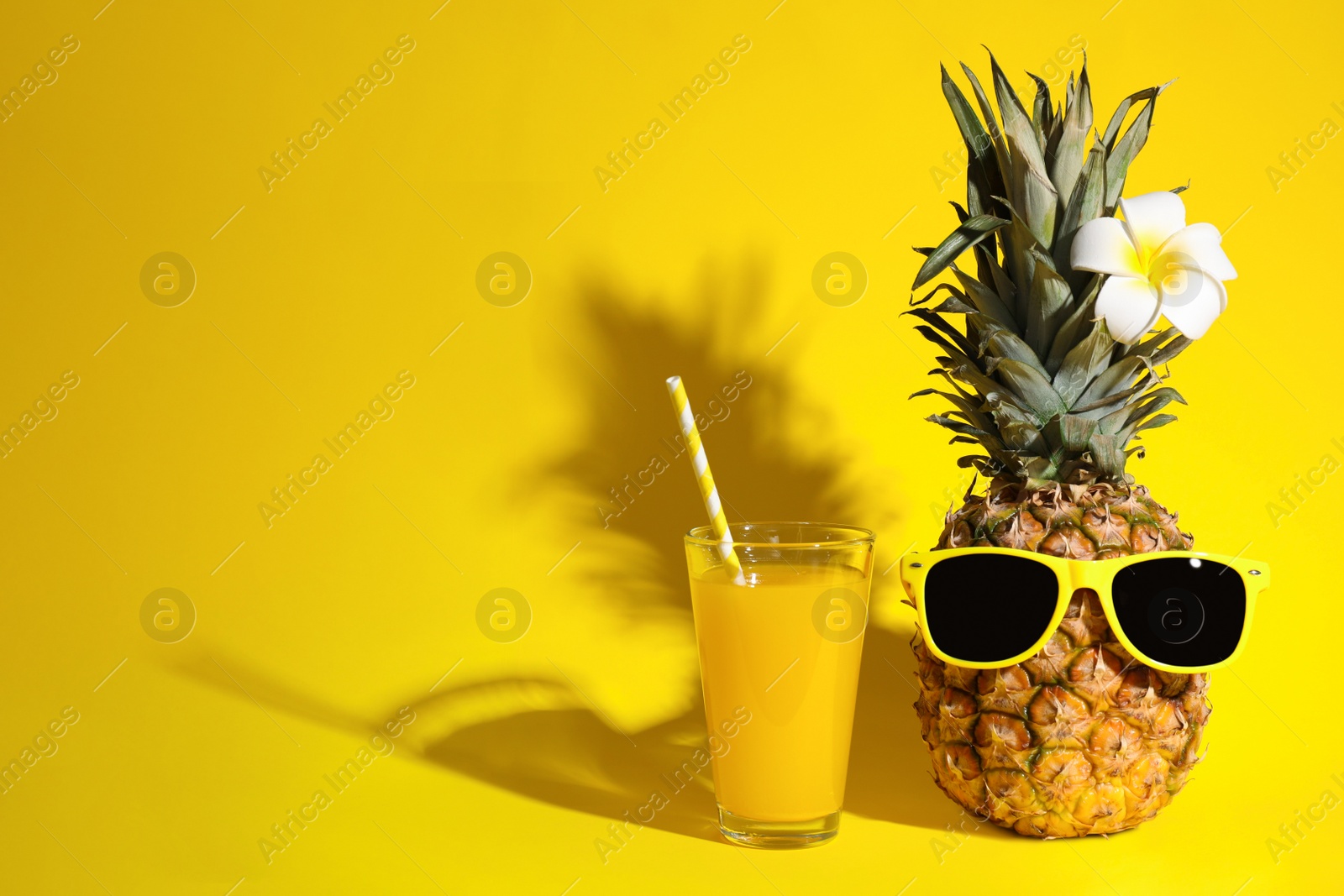 Photo of Glass of fresh pineapple juice and fruit with sunglasses on yellow background, space for text