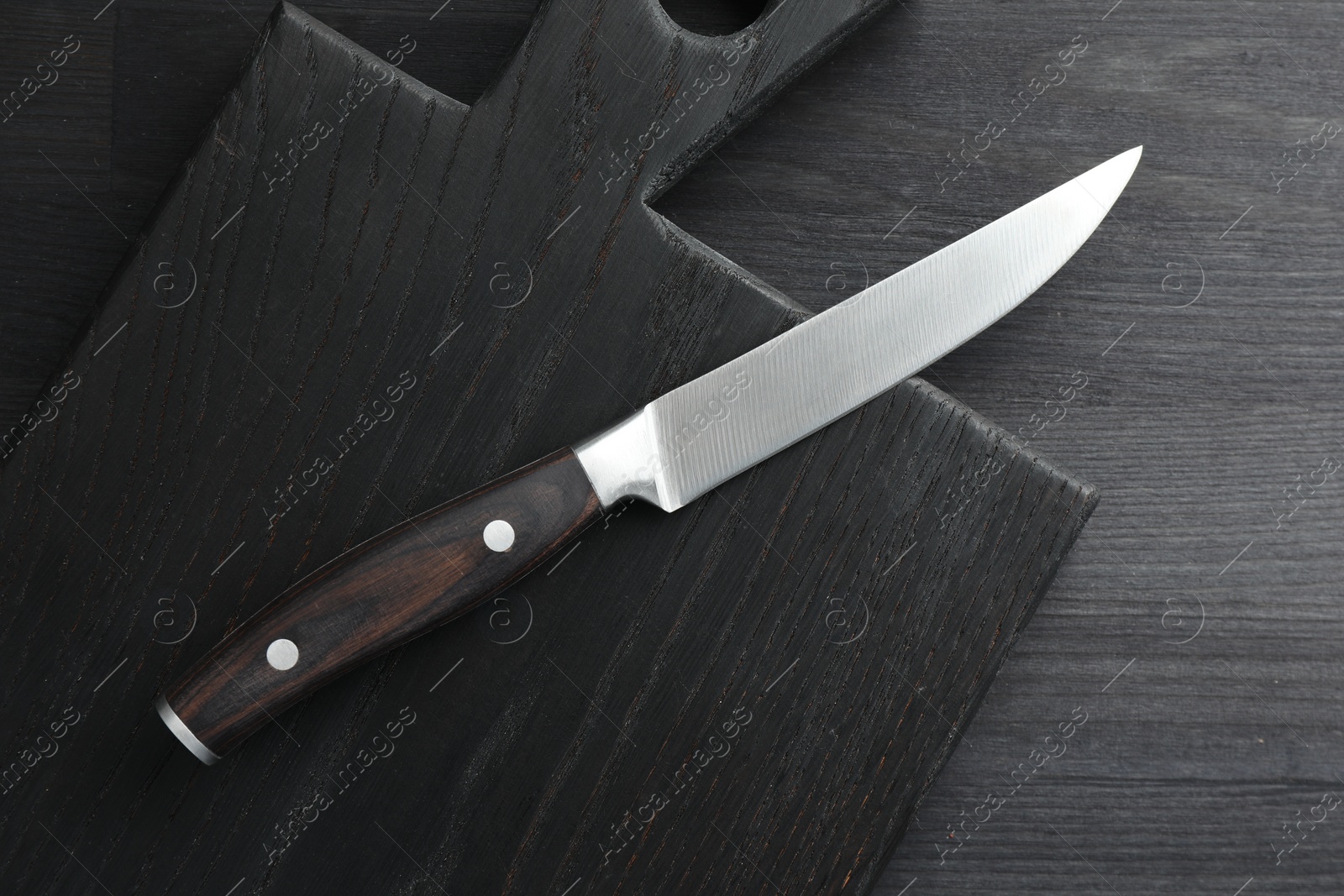 Photo of One sharp knife and board on black wooden table, top view