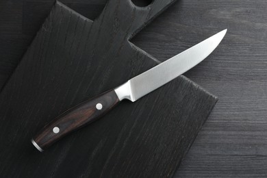 Photo of One sharp knife and board on black wooden table, top view