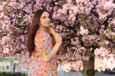 Beautiful woman with straw hat near blossoming tree on spring day