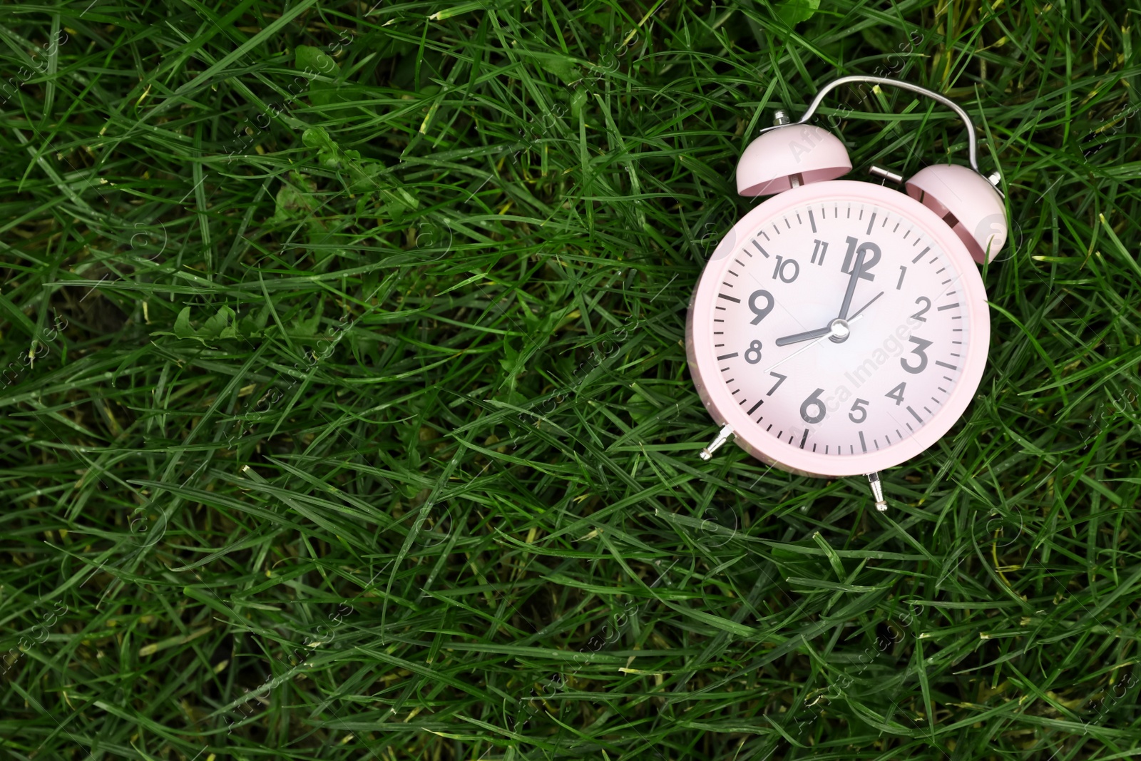 Photo of Pink small alarm clock on green grass outdoors, top view. Space for text