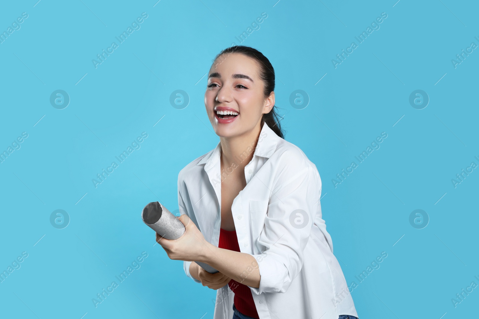 Photo of Young woman blowing up party popper on light blue background