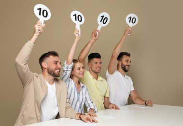 Photo of Panel of judges holding signs with highest score at table on beige background