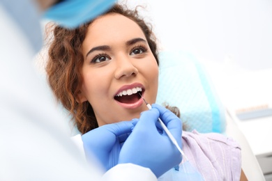 Dentist examining African-American woman's teeth with probe in hospital