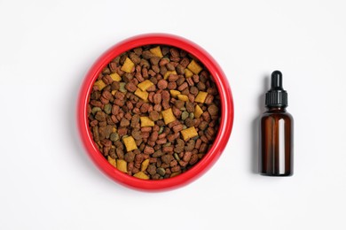 Photo of Glass bottle of tincture near dry pet food in bowl on white background, top view