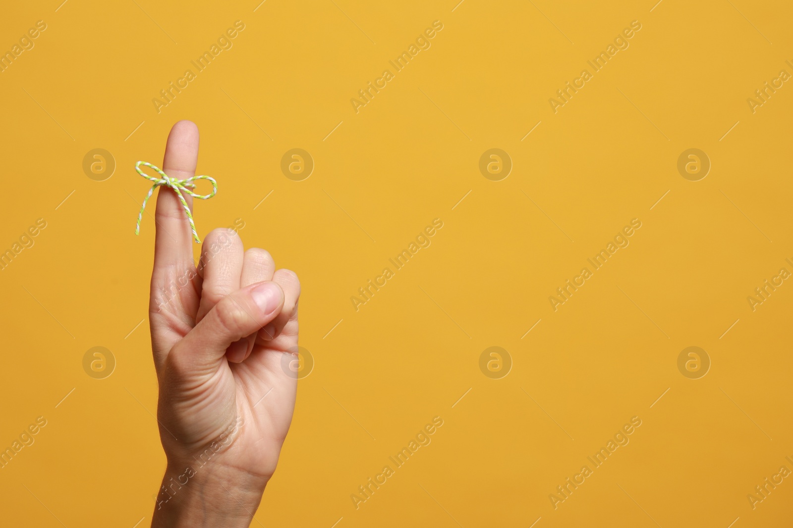 Photo of Woman showing index finger with tied bow as reminder on orange background, closeup. Space for text