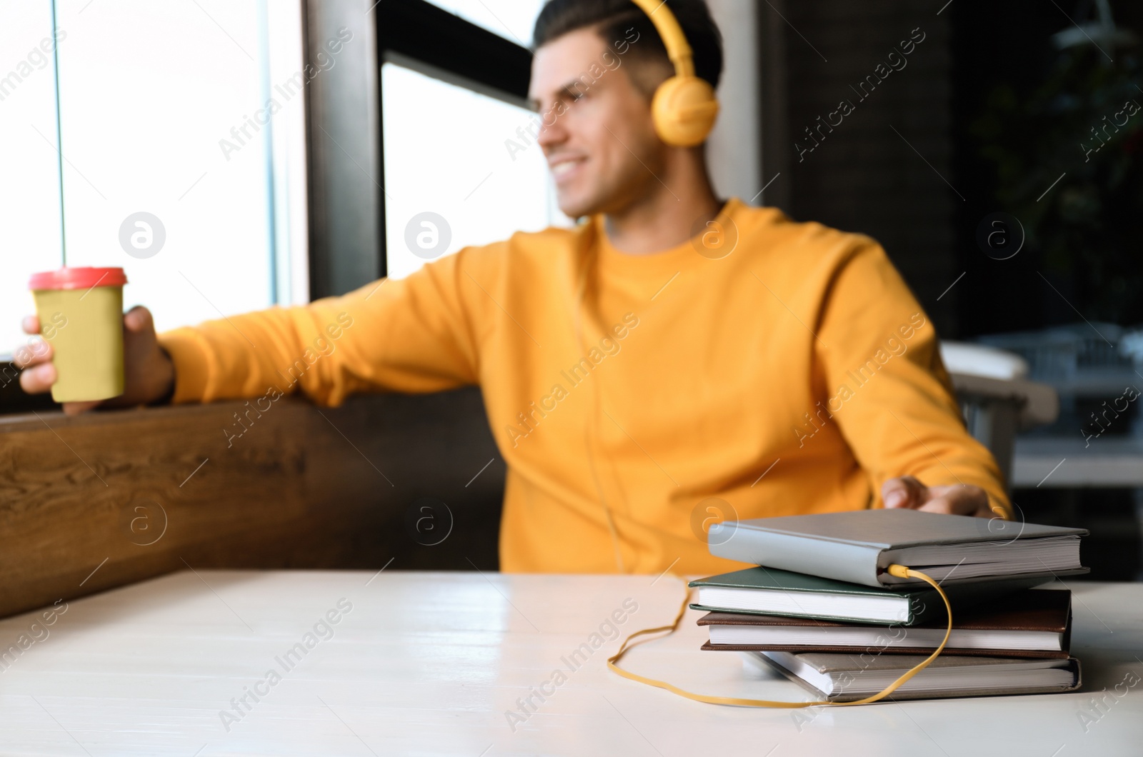 Photo of Man with headphones connected to book at table in cafe