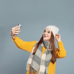 Photo of Beautiful young woman in warm clothes  taking selfie on grey background. Winter season