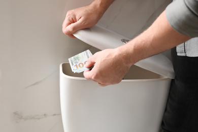 Photo of Man hiding money in toilet tank indoors, closeup. Financial savings